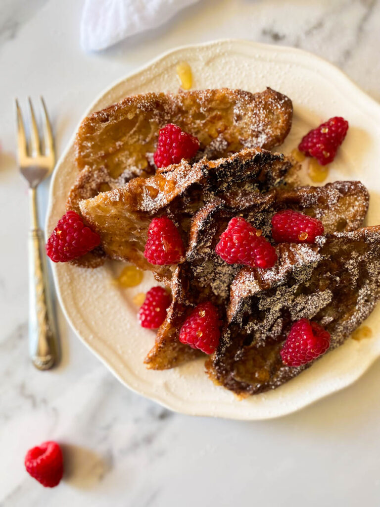 close up croissant with raspberry, icing sugar and maple syrup on a plate, fork on the side