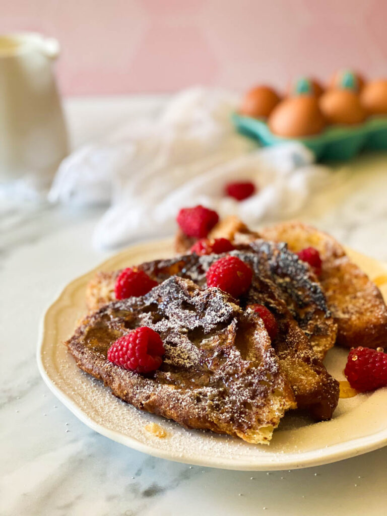 plate of croissant pain perdu with raspberries, in the back, eggs, towel and milk 