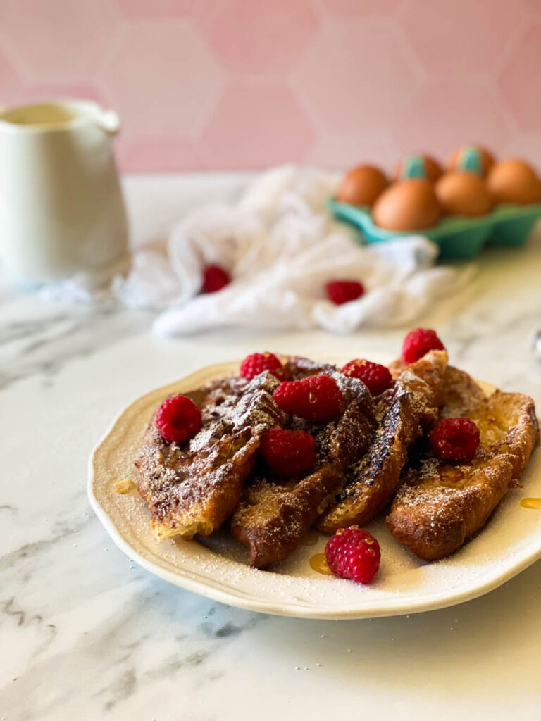 plate of croissant pain perdu with raspberries, in the back, eggs, towel and milk jug