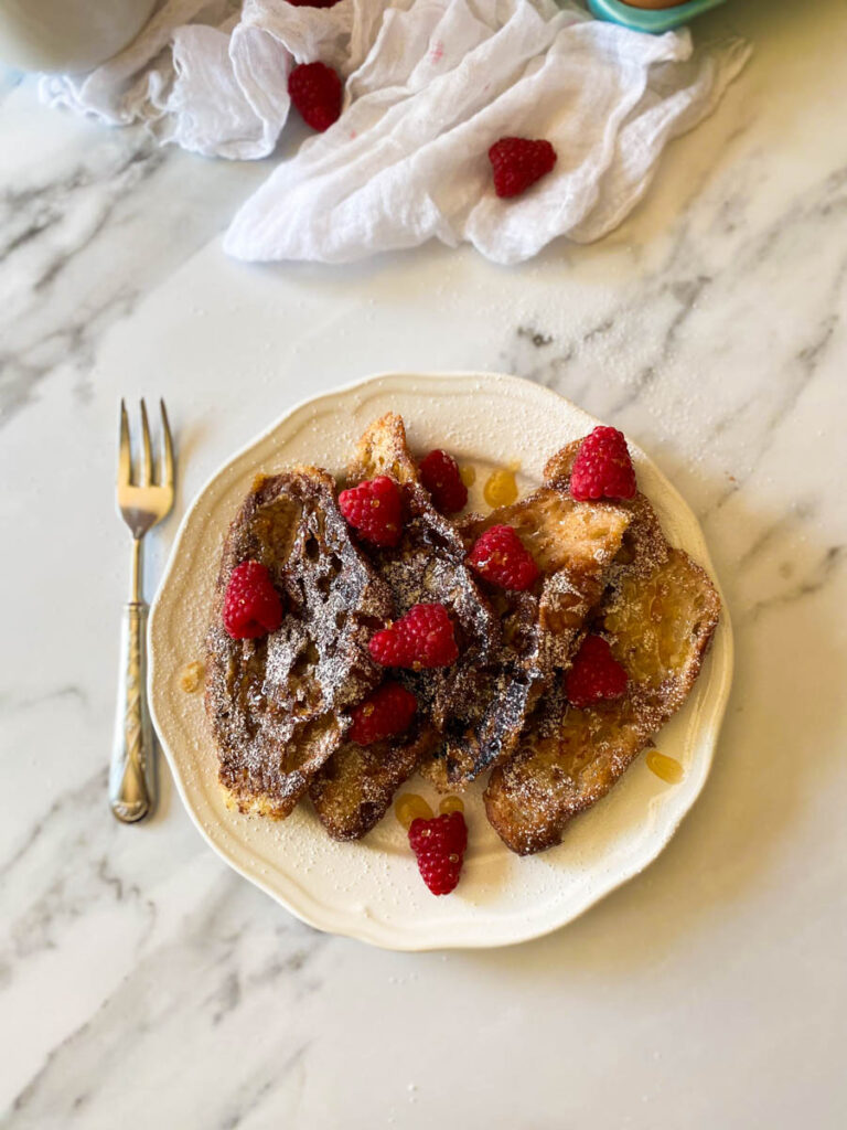 plate of croissant pain perdu with raspberries,fork, towel from top