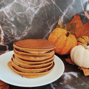 pumpkin pie spice pancakes on a plate, pumpkin and leaves on the side, on a black marble
