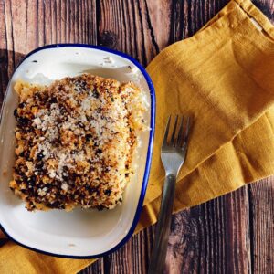 Pancetta Mac & Cheese With Cheesy Garlic Panko 2 from top pancetta mac & cheese in a blue rimmed bowl, under a yellow towel and fork, on a wooden background