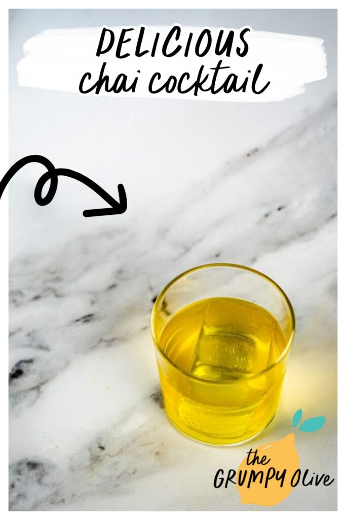 4 Ingredient Chai Cocktail, Delicious & Easy 4 This image features a chai cocktail with a rich yellow hue, served in a glass over a large clear ice cube. The drink sits on a light marbled surface, highlighting the warm, inviting tones of the chai-inspired beverage.