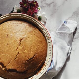 almond cake on a dish, a napkin under and flowers on side, on a marble background