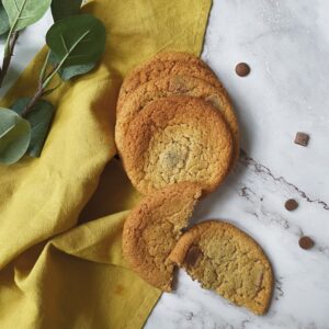 chocolate chip cookies sitting on a yellow napkin with chocolate chips on the side and some leaves