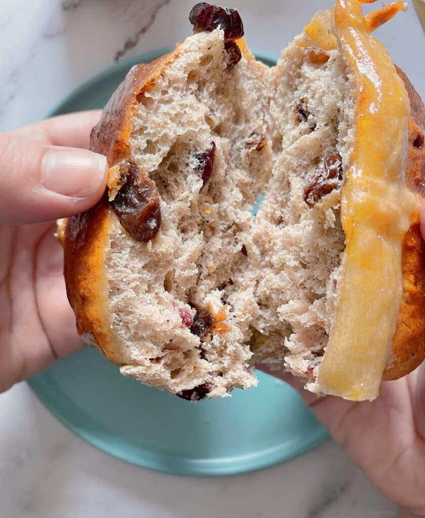 brioche Hot Cross Buns on a wooden board with a cup of coffee and a single bun on a light blue dish with a golden knife