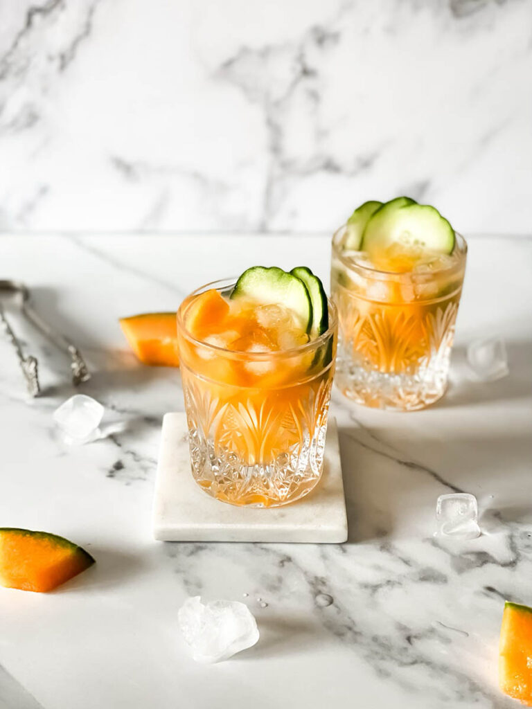 Delicious Melon Gin Cocktail with Cucumber 4 melon gin cocktails in two glasses wiith ice, cucumber slices and melon balls over a marble ground