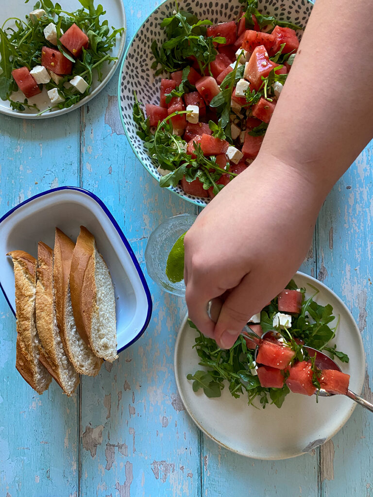 Easy Watermelon and Feta Salad Recipe 3 watermelon feta salad in three plates and a side of bread, a hand mixing the salad
