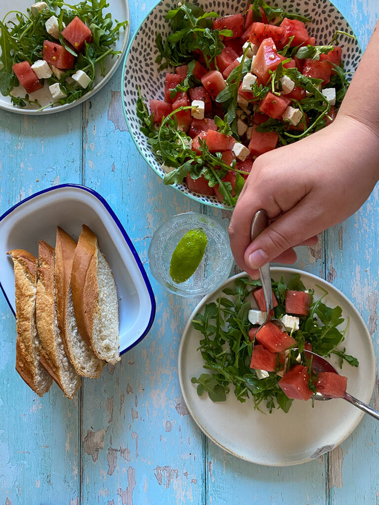 Easy Watermelon and Feta Salad Recipe 4 watermelon feta salad in plates and a side of bread, a hand mixing the salad, picture from above