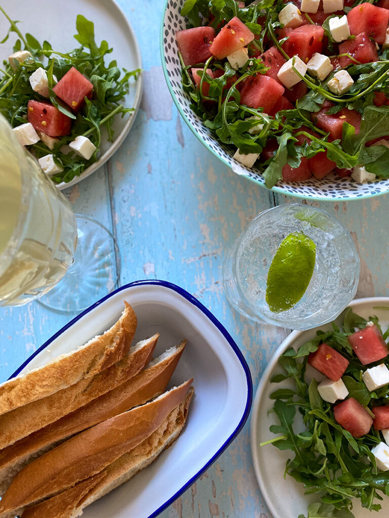 Easy Watermelon and Feta Salad Recipe 1 watermelon and feta salad recipe, two glasses of drinks beside, on a light blue wooden board