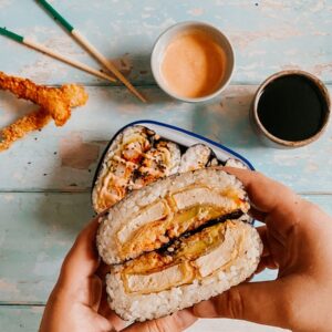 Easy Onigirazu - Japanese Rice Sandwiches 3 hand holding an onigirazu sandwich, more sandwiches in a bowl, prawn katsu, sauce and chopsticks