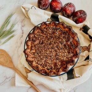 plum streusel pie seen from above, napkin and plums on the side, wooden spoon