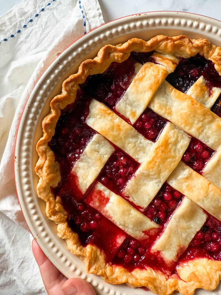 Delicious Bourbon & Mixed Berries Pie, #1 Christmas Dessert 7 A mixed berries pie with a beautifully browned lattice crust sits on a marble surface with a folded white cloth nearby, viewed from above.