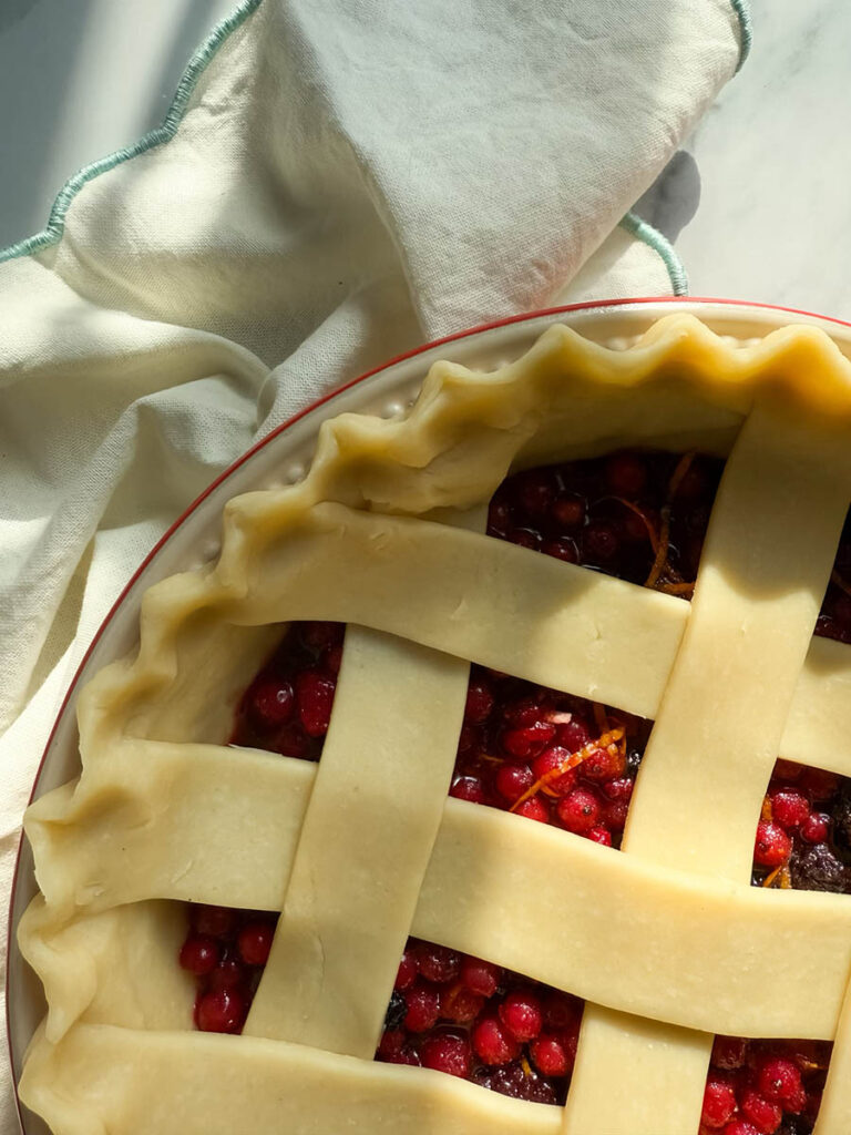 Delicious Bourbon & Mixed Berries Pie, #1 Christmas Dessert 3 Close-up of an unbaked mixed berries pie, highlighting the vibrant red berries beneath the crisscrossed lattice crust, with a soft cloth draped beside it.