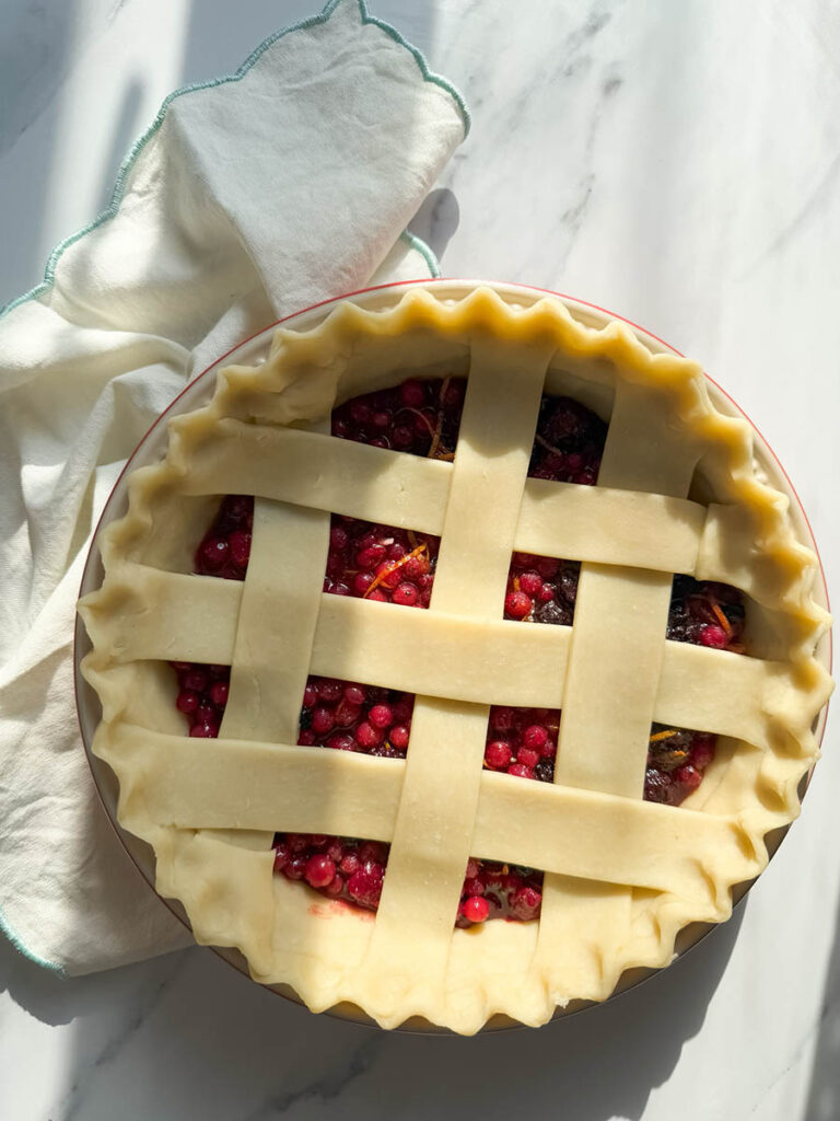 Delicious Bourbon & Mixed Berries Pie, #1 Christmas Dessert 2 an unbaked mixed berries pie, highlighting the vibrant red berries beneath the crisscrossed lattice crust, with a soft cloth draped beside it.