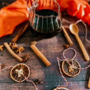 Gingerbread Syrup Recipe For A Delicious Christmassy Gingerbread Latte 2 from front - gingerbread syrup in a jug, spoon, star anise, orange slices and cinnamon sticks around, twine, spoons and a red towel on the sides. over a wooden background