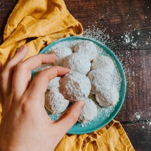 Kourabiethes, Delicious & Vegan Greek Cookies 2 kourabiethes cookies on a blue plate and yellow napkin, a hand with a cookie