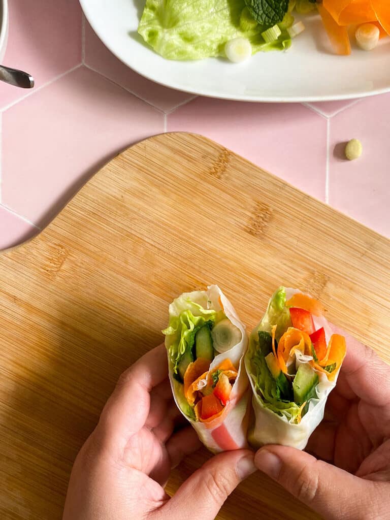 Vegan Rice Paper Rolls With Yummy Peanut Dipping Sauce 10 vegan rice paper rolls with a peanut dipping sauce in a white bowl with a spoon on a wooden board