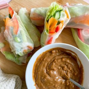rice paper rolls with vegetables on a wooden board, with peanut dip on the side