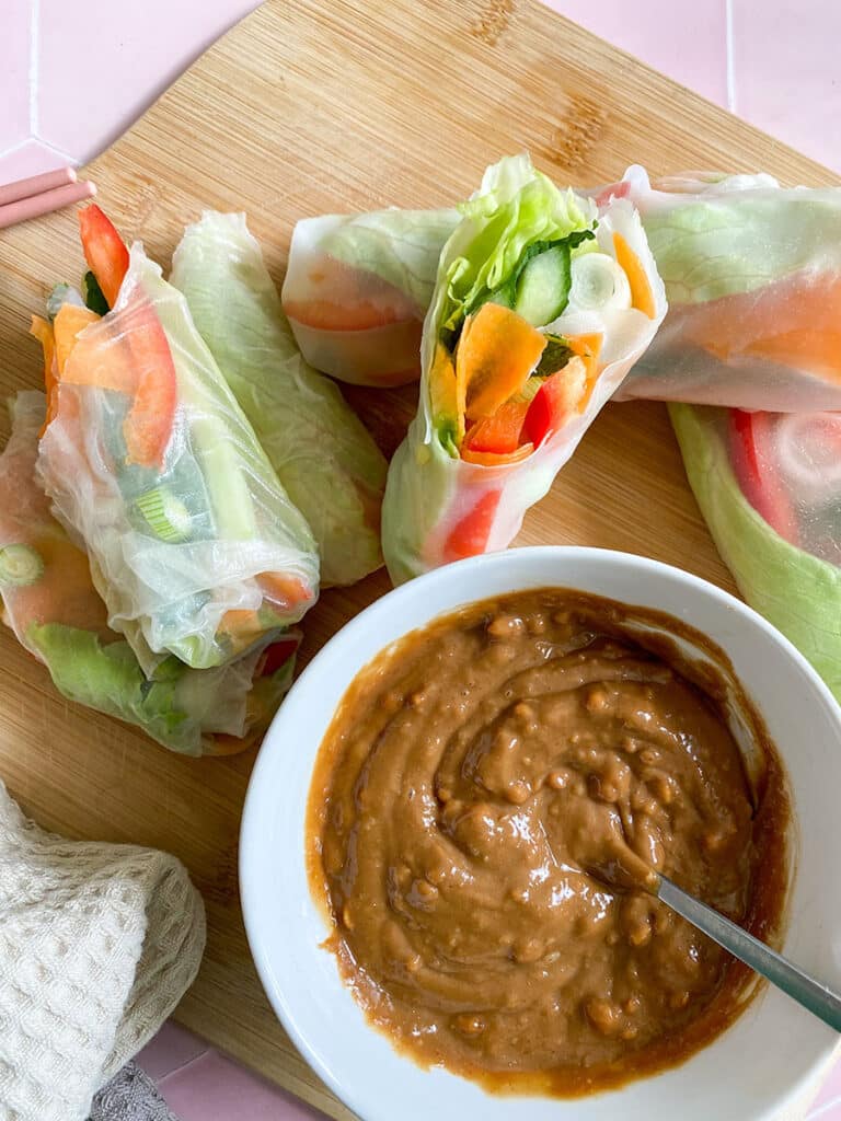 Vegan Rice Paper Rolls With Yummy Peanut Dipping Sauce 1 vegan rice paper rolls with a peanut dipping sauce in a white bowl with a spoon on a wooden board