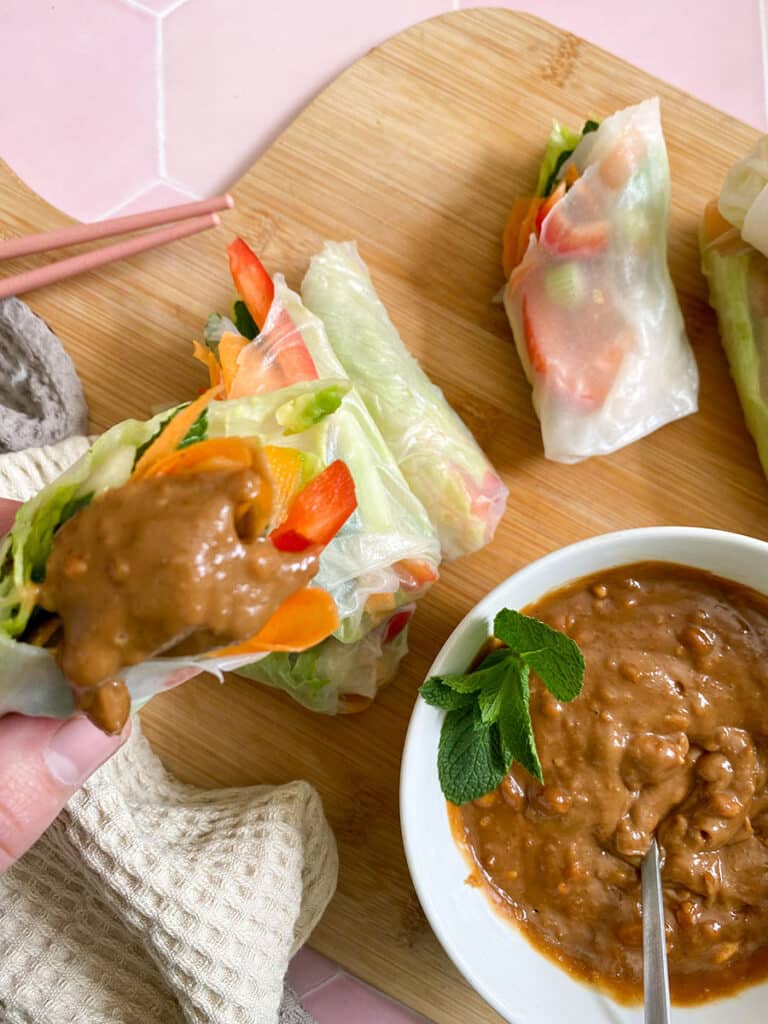 Vegan Rice Paper Rolls With Yummy Peanut Dipping Sauce 7 vegan rice paper rolls with a peanut dipping sauce in a white bowl with a spoon on a wooden board