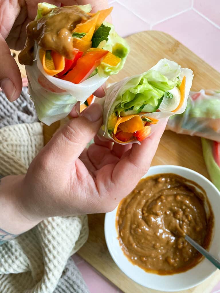 Vegan Rice Paper Rolls With Yummy Peanut Dipping Sauce 9 vegan rice paper rolls with a peanut dipping sauce in a white bowl with a spoon on a wooden board