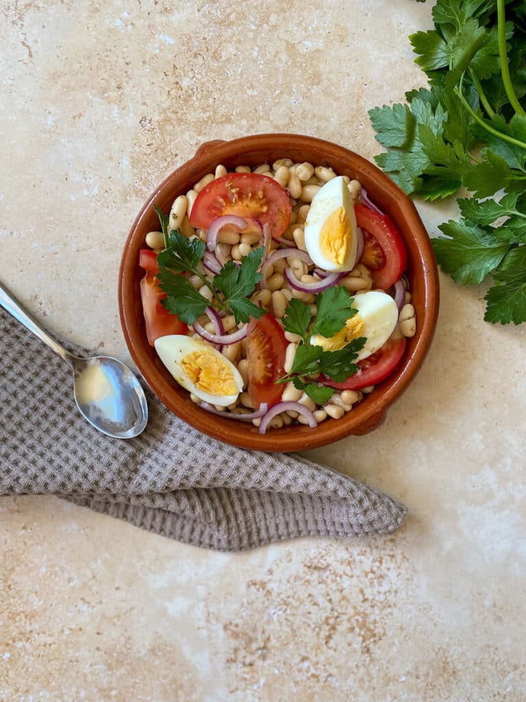 10 Minutes Summer Butter Beans Salad 3 spoon on a towel a tomato, under a bowl of butter beans salad and parsley