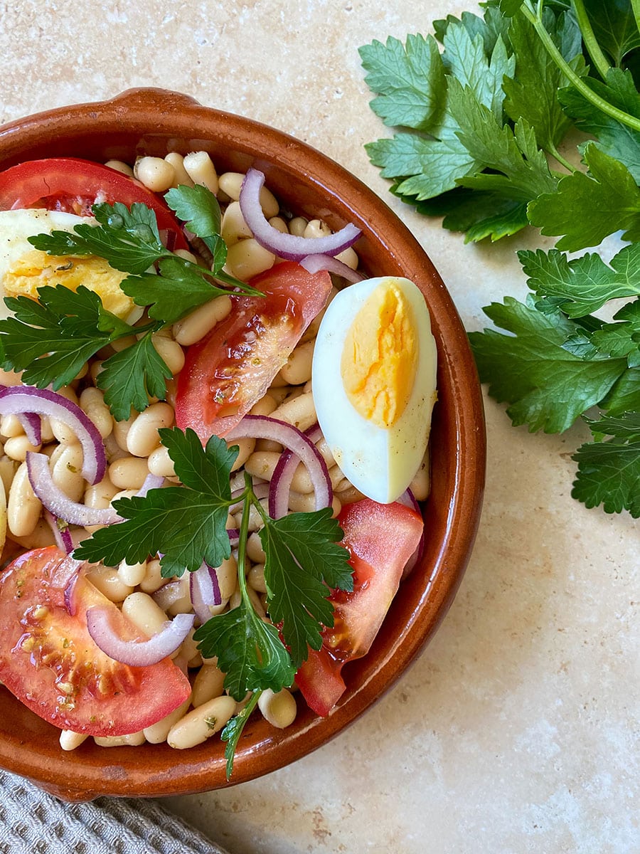 close up, bean salad in a bowl with eggs and tomatoes, parsley on the background and a napkin