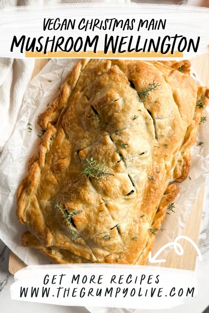 A golden-brown vegan mushroom Wellington on a sheet of parchment paper, garnished with fresh thyme, with a rustic kitchen towel and onion peels in the background.