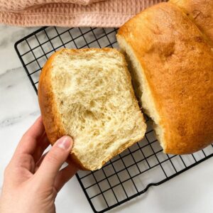 vegan brioche on a cookie rack and pink napkin, hand holding a slice on the rack