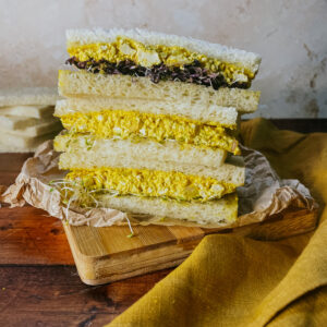 vegan egg mayo sandwich on a wooden board, a yellow napkin on the side, slice of bread on the back