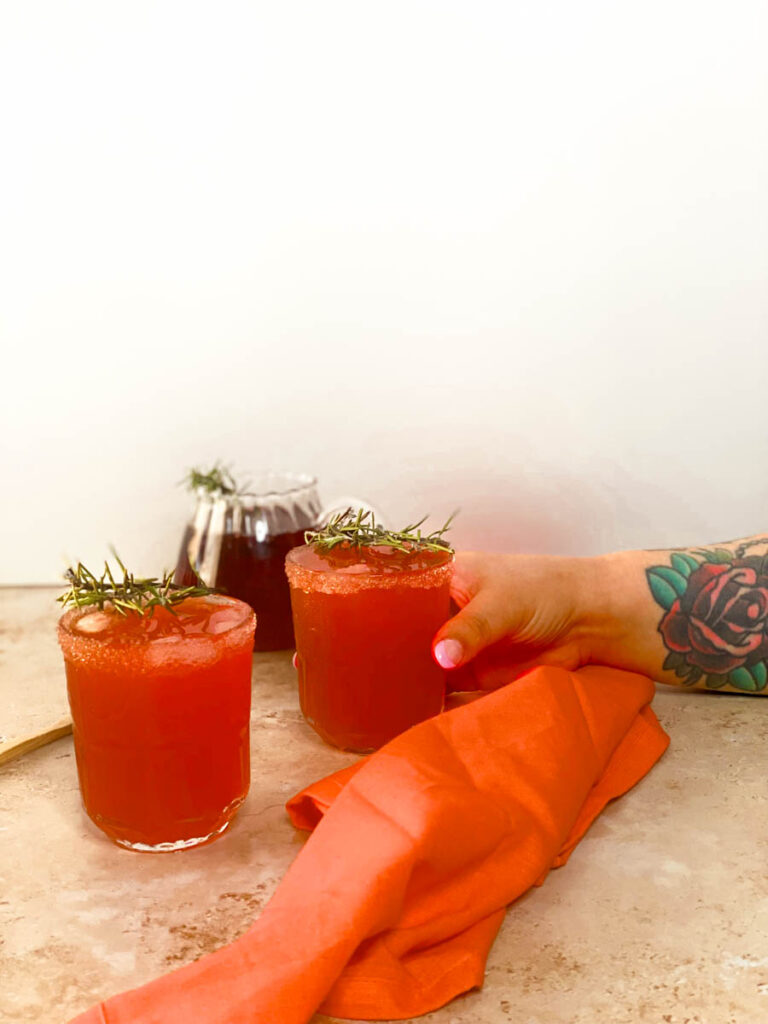 5 Minutes Love Potion Cocktail Recipe 2 hand holding a glass of love potion cocktail with rosemary as garnish, beside a red towel