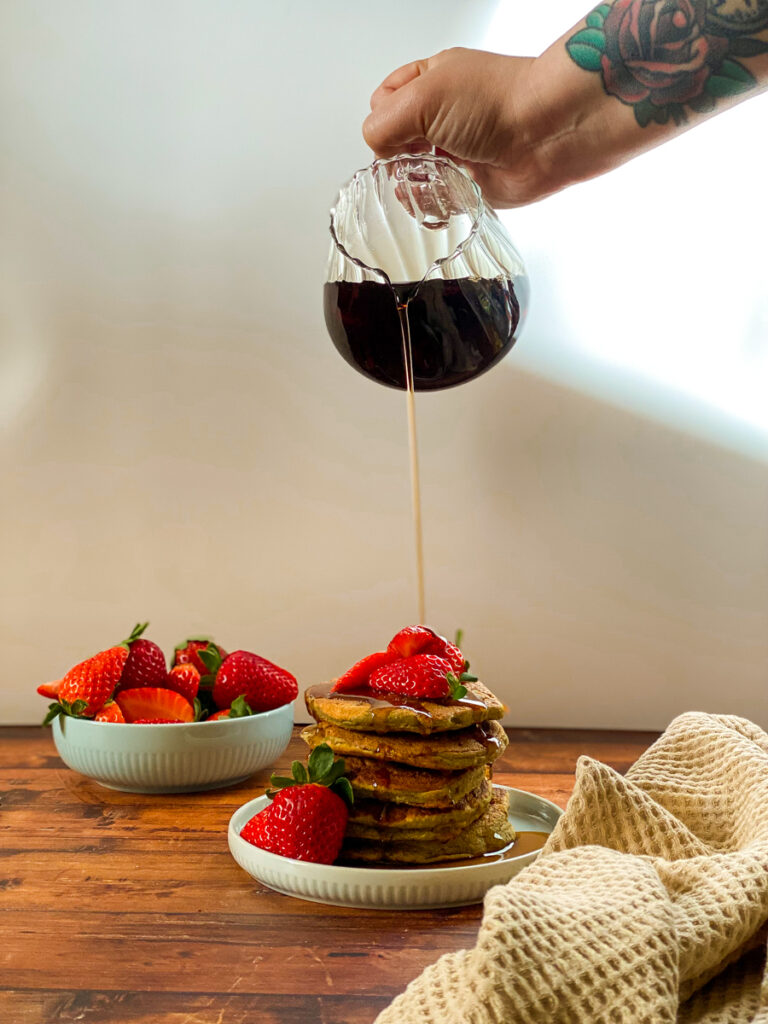 30 Family Friendly Vegan Recipes So Delicious You Must Try 1 hand pouring maple syrup on a stack of pancakes with strawberries, plate with strawberries behind