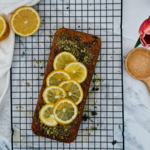 lemon pistachio loaf on a cookie rack, wooden board on the background and flowers, from above