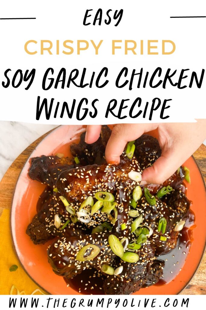 Best Crispy Fried Soy Garlic Chicken Wings Recipe 7 hand reaching for a wing on a plate of soy garlic chicken wings - pin image