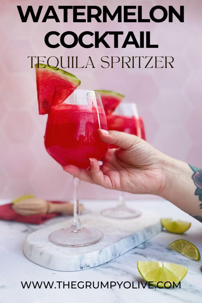 watermelon tequila spritzer served in two wine glasses, being held by a hand, sitting on a marble slate with a slice of watermelon each and some lime wedges scattered around