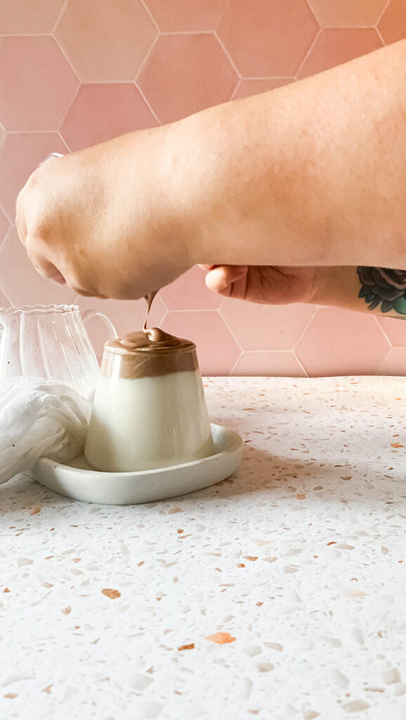 dalgona chocolate recipe in a glass with milk being filled, on a marble tray with a glass jar filled with milk in the background