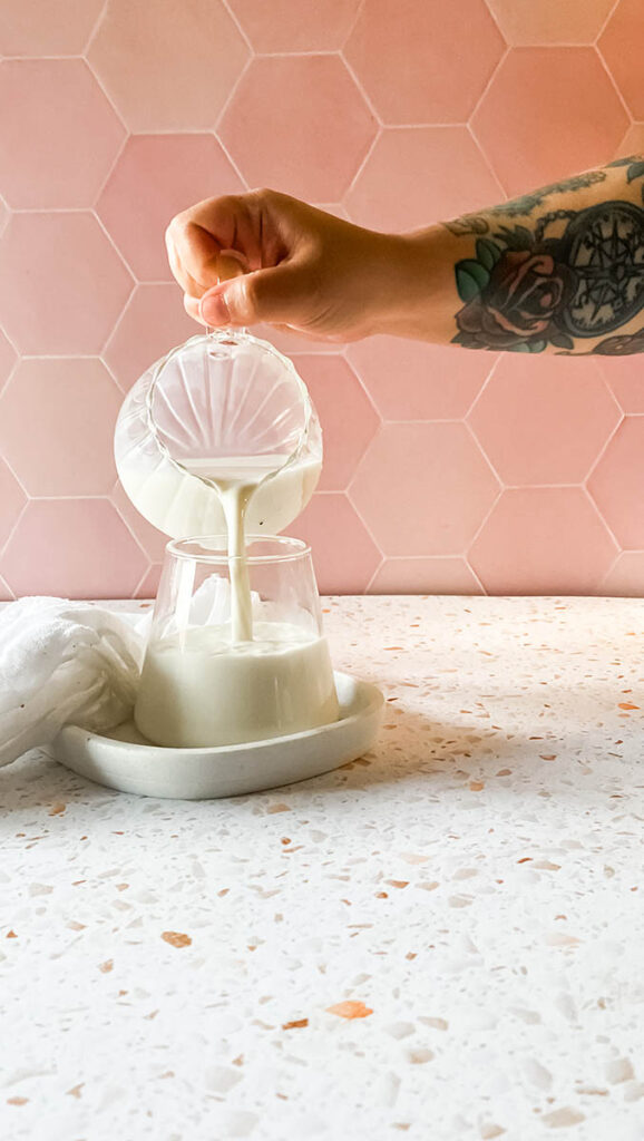 a glass being filled with milk from a glass jar, sitting on a marble tray