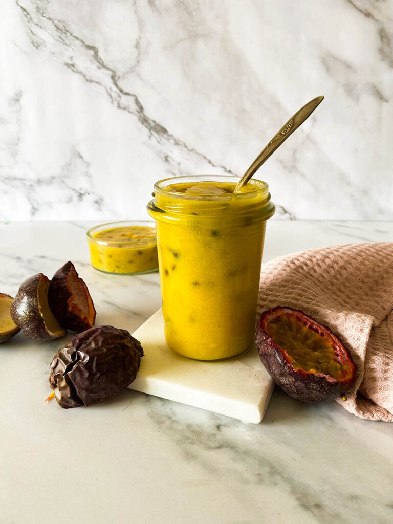 Passion Fruit Curd: Easy & Delicious 3 passion fruit curd jar on a marble background with a vintage spoon, with fresh passion fruits over a pink napkin