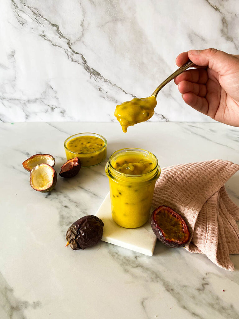 Passion Fruit Curd: Easy & Delicious 6 passion fruit curd jar on a marble background with a vintage spoon, with fresh passion fruits over a pink napkin
