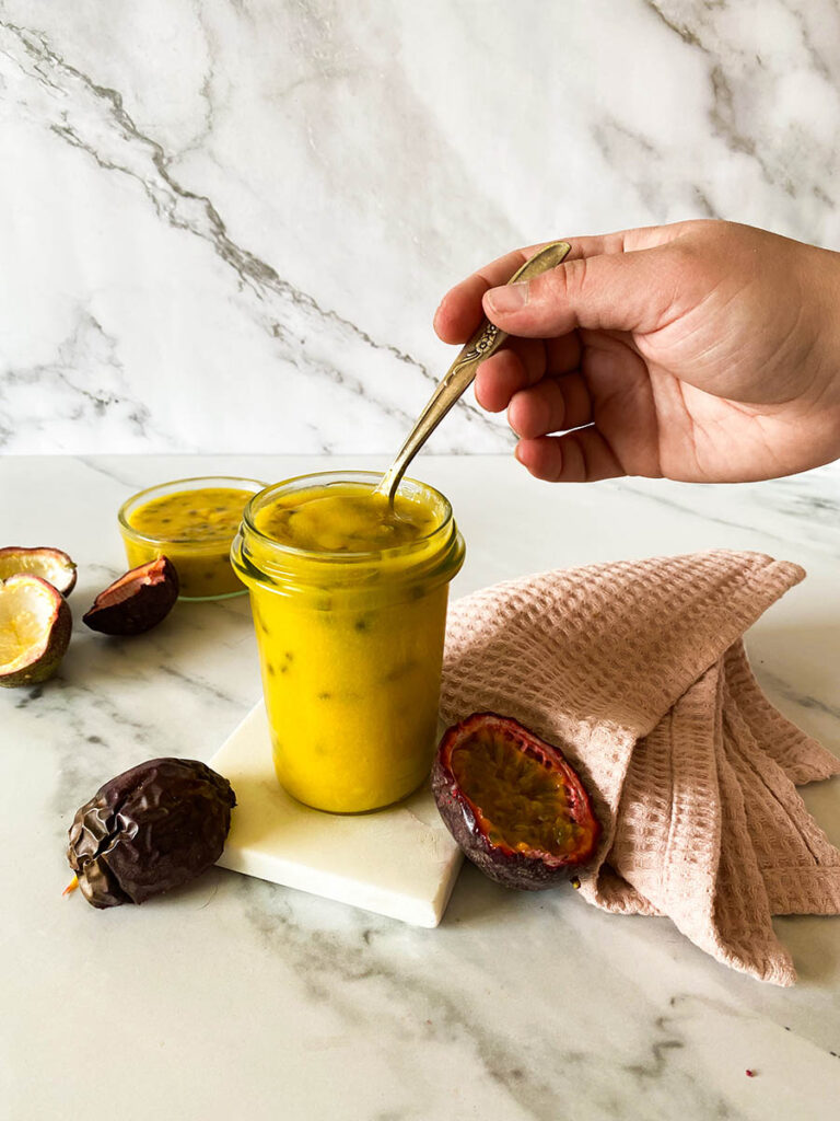 Passion Fruit Curd: Easy & Delicious 7 passion fruit curd jar on a marble background with a vintage spoon, with fresh passion fruits over a pink napkin
