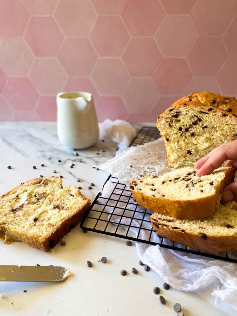 Delicious Fluffy Chocolate Chip Brioche Recipes 2 wire rack with chocolate chip brioche on, hand reaching in for a slice
