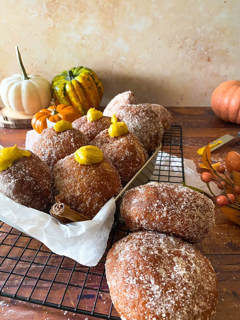 The Best Pumpkin Cheesecake Donuts: Perfect Fall Treat 2 pumpkin cheesecake donut recipe, donuts seen from the front in a metal container, over a cooling rack