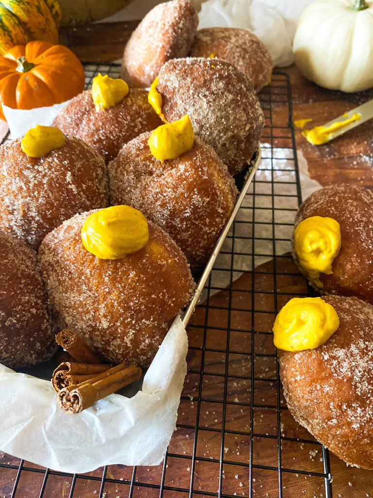 The Best Pumpkin Cheesecake Donuts: Perfect Fall Treat 11 pumpkin cheesecake donut recipe, donuts seen from the front in a metal container over a cooling rack
