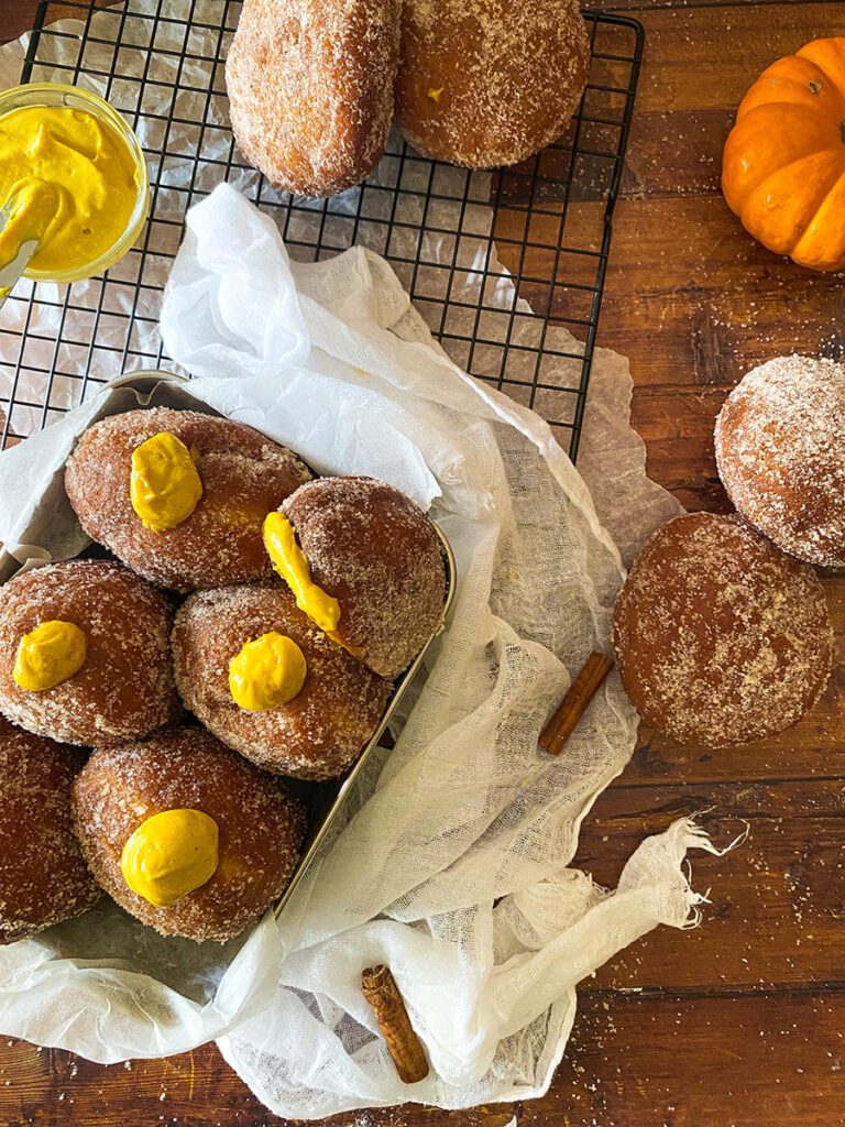 The Best Pumpkin Cheesecake Donuts: Perfect Fall Treat 4 pumpkin cheesecake donut recipe, donuts seen from above in a metal container over a cooling rack