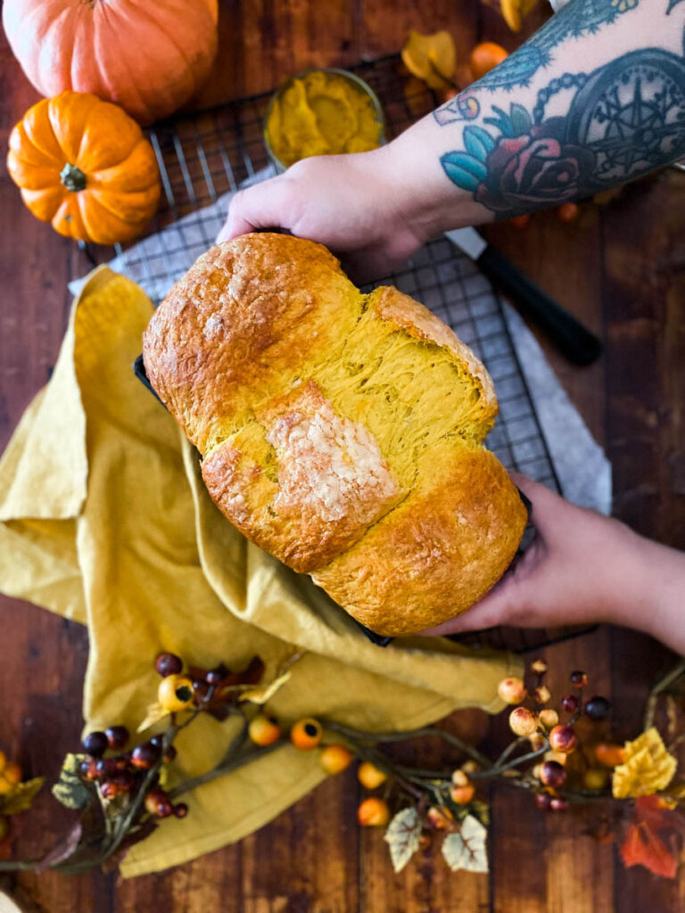 Easy Pumpkin Brioche Recipe - Fall Breakfast Staple 4 hands reaching pumpkin brioche on a yellow towel, on a wire rack, wood background