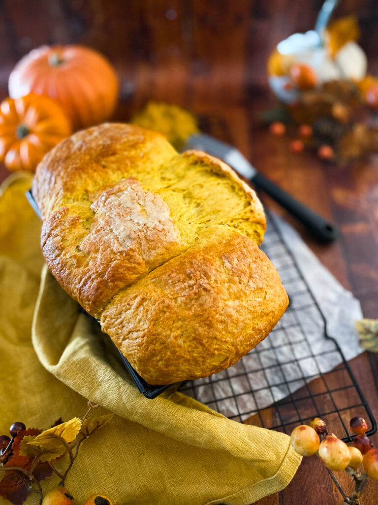 Easy Pumpkin Brioche Recipe - Fall Breakfast Staple 1 pumpkin brioche on a yellow towel, on a wire rack, wood background, pumpkins around