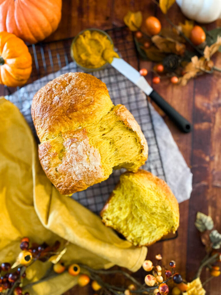 Easy Pumpkin Brioche Recipe - Fall Breakfast Staple 3 pumpkin brioche on a yellow towel, on a wire rack, wood background, from top