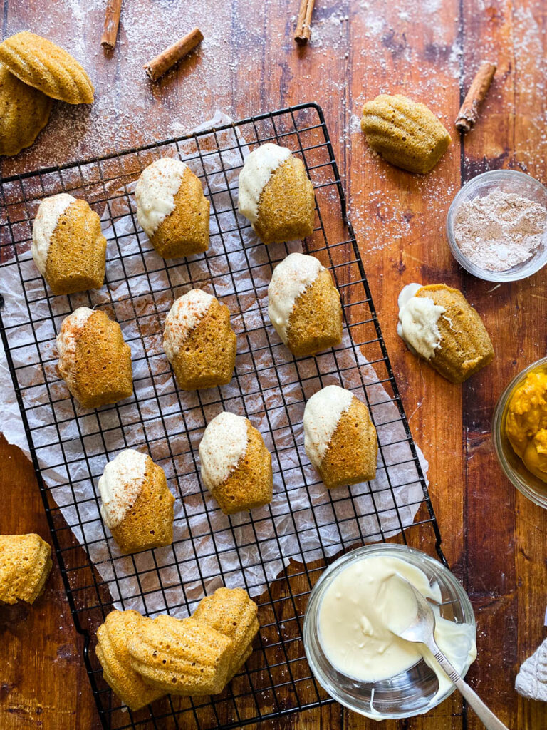 Delicious Pumpkin Madeleines With White Chocolate 5 from above pumpkin madeleines on a cooling rack on a wooden background