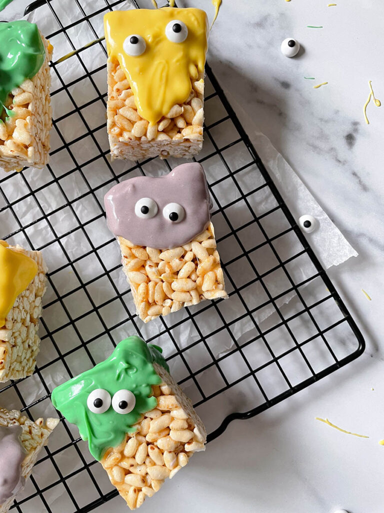 MM Rice Krispie Treats - The Delicious Monster Mash Treats 5 MM rice krispie treats on a cooling rack with pumpkins scattered around
